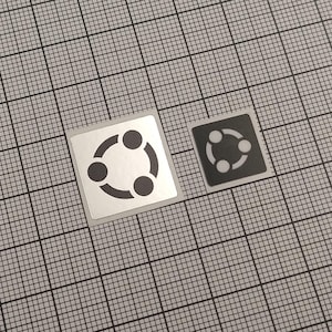 Könnte beinhalten: Zwei quadratische Aufkleber mit einem kreisförmigen Design aus drei verbundenen Punkten. Einer ist silberfarben mit schwarzen Punkten, der andere ist schwarz mit weißen Punkten. Sie befinden sich auf einem grauen Rasterhintergrund.