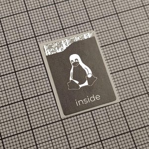 May include: A rectangular sticker with a gray background and a white penguin logo. The word "inside" is printed in white at the bottom. The sticker is on a gray grid surface.