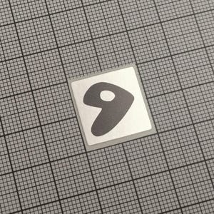 May include: A small, square sticker with a gray number nine on a white background. The number has a rounded shape with a small white circle inside. The sticker is set against a gray grid background.