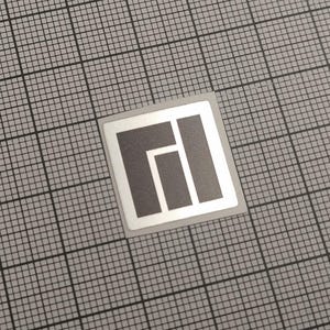 Könnte beinhalten: Ein quadratischer Aufkleber mit einem grau-weißen geometrischen Design. Das Design zeigt einen grauen Block mit weißem Rand und drei grauen Rechtecken im Inneren. Der Aufkleber befindet sich auf einem grauen Gitterhintergrund.
