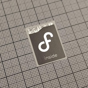 Könnte beinhalten: Ein rechteckiger Aufkleber mit dunkelgrauem Hintergrund und einem weißen "f"-Symbol. Das Wort "inside" steht in Weiß unter dem Symbol. Der Aufkleber befindet sich auf einem grauen Gitterhintergrund.