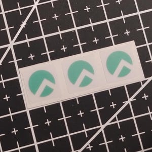 May include: A strip of three square stickers, each featuring a circular mint green design with a white mountain-like peak shape cut out from the center. The stickers are arranged horizontally on a white backing sheet.