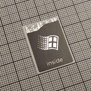 Pode incluir: Um autocolante retangular com fundo preto e logótipo Windows branco. A palavra "inside" está impressa em branco abaixo do logótipo. O autocolante está sobre um fundo de grelha cinzenta.
