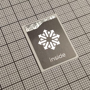 Könnte beinhalten: Ein rechteckiger schwarzer Aufkleber mit einem weißen geometrischen Design und dem Wort "inside" in Weiß. Der Aufkleber befindet sich auf einem Rasterhintergrund.