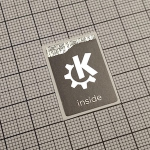 Könnte beinhalten: Ein rechteckiger, dunkelgrauer Aufkleber mit einem weißen Zahnrad und dem Buchstaben "K" darin. Das Wort "inside" ist unter dem Logo aufgedruckt. Der Aufkleber befindet sich auf einem grauen Rasterhintergrund.
