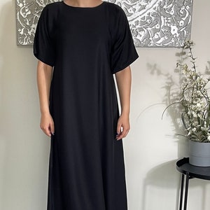 Può includere: Un abito maxi nero con maniche corte e scollo rotondo. L'abito è realizzato in un tessuto morbido e fluido e ha un design semplice ed elegante.