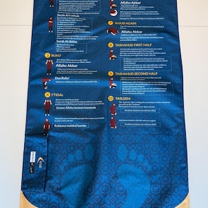 May include: Blue prayer mat with detailed instructions for prayer, including diagrams and Arabic text. The mat features a geometric pattern and a beige border. The text includes steps like 'Make Your Intention To Pray' and 'Tasleem'.