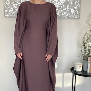 May include: A long, flowing, mauve-colored abaya with a loose, comfortable fit. The abaya has a round neckline and long sleeves.