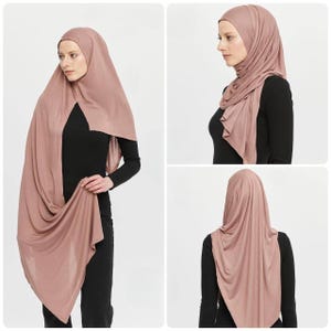 May include: A dusty rose coloured hijab with a long, flowing design. The hijab is draped over the shoulders and head, with the ends tucked in at the neck. The hijab is made of a soft, lightweight fabric.