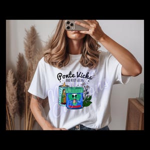 Könnte beinhalten: Weißes T-Shirt mit dem Text "Ponte Kicks and Keep Going" über einer Grafik einer Kerze und eines Glases mit einer Cartoonfigur. Das T-Shirt wird von einer Person getragen.