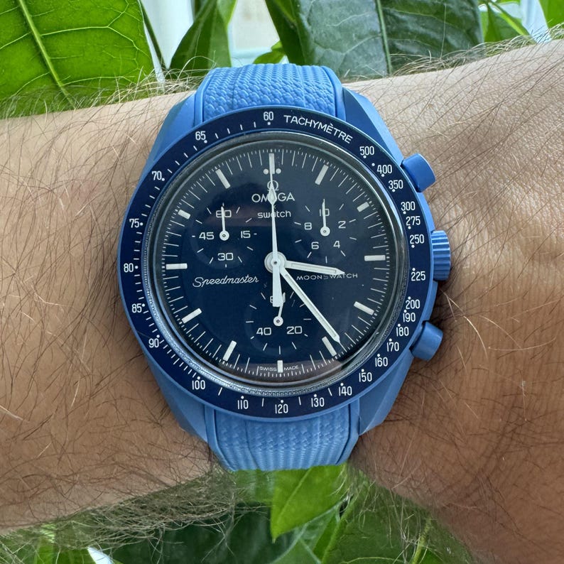 May include: A blue Omega Speedmaster MoonSwatch watch with a dark blue dial and white hands. The watch has a blue bezel with a tachymeter scale and a blue rubber strap. The watch case measures approximately 42mm.
