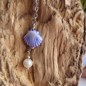 Op de afbeelding: Een zilveren ketting met een blauwe en witte schelpbedel en een witte parelbedel.