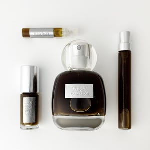 K&ouml;nnte beinhalten: Eine Sammlung von Parf&uuml;mbeh&auml;ltern, bestehend aus einer gro&szlig;en, abgerundeten Glasflasche und drei kleineren zylindrischen Fl&auml;schchen. Jeder Beh&auml;lter ist mit einer dunkelbraunen Fl&uuml;ssigkeit gef&uuml;llt und tr&auml;gt ein silbernes Etikett mit dem Text Green Smoke Lucky Cloud.