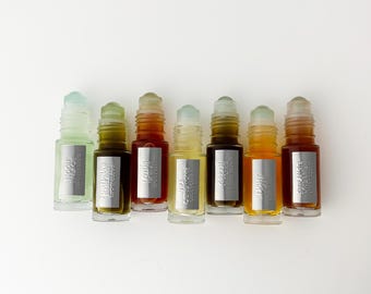 Könnte beinhalten: Sieben kleine Glasfläschchen mit Roll-on-Aufsatz in einer Reihe, die jeweils eine unterschiedlich gefärbte Flüssigkeit von hellgrün bis dunkel bernsteinfarben enthalten. Jede Flasche hat ein silbernes rechteckiges Etikett mit Text.