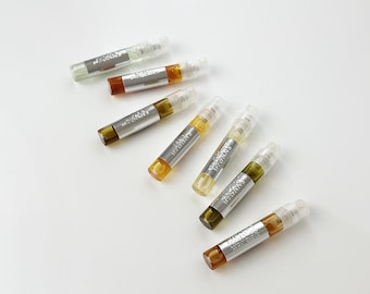 Könnte beinhalten: Sechs kleine zylindrische Glassprühfläschchen mit Flüssigkeiten in verschiedenen Bernstein-, Gold- und Hellgrüntönen. Jedes Fläschchen hat ein silberfarbenes Etikett mit aufgedrucktem Text und eine transparente Sprühkappe aus Kunststoff.