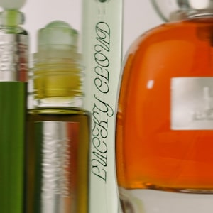 K&ouml;nnte beinhalten: Eine Sammlung von Glasparf&uuml;mflaschen, darunter eine hohe, d&uuml;nne Flasche mit dem in Gr&uuml;n gedruckten Text Lucky Cloud, eine kleine Roll-on-Flasche mit dunkel bernsteinfarbener Fl&uuml;ssigkeit und eine gro&szlig;e, abgerundete Flasche mit leuchtend orangefarbener Fl&uuml;ssigkeit.