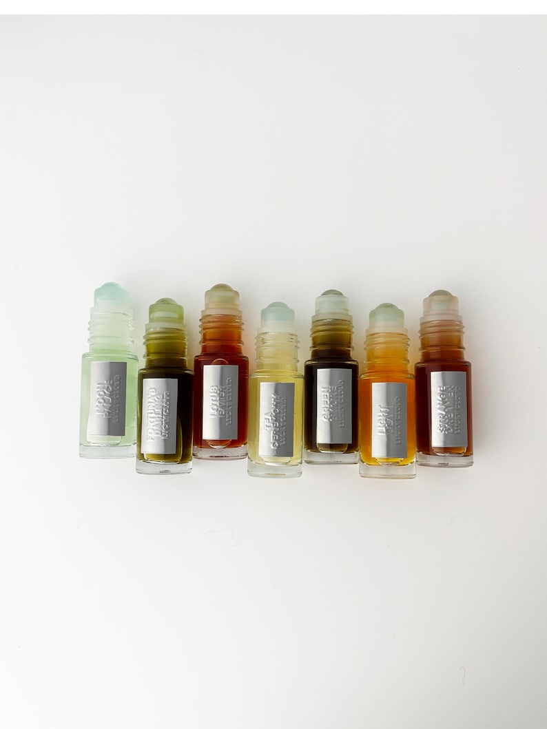 K&ouml;nnte beinhalten: Sieben kleine Glasfl&auml;schchen mit Roll-on-Aufsatz in einer Reihe, die jeweils eine unterschiedlich gef&auml;rbte Fl&uuml;ssigkeit von hellgr&uuml;n bis dunkel bernsteinfarben enthalten. Jede Flasche hat ein silbernes rechteckiges Etikett mit Text.