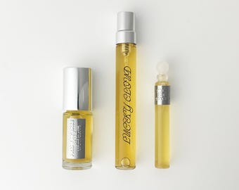 Könnte beinhalten: Drei Glasparfümflaschen mit goldener Flüssigkeit. Die linke Flasche ist kurz mit silbernem Verschluss und Etikett FRANKINCENSE. Die mittlere Flasche ist hoch mit silbernem Sprühkopf und Text LUCKY CLOUD. Die rechte Flasche ist schmal.