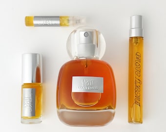 May include: A collection of three amber-colored perfume bottles labeled Lucky Cloud. The set includes a large rounded glass bottle with a silver cap, a small cylindrical rollerball bottle, and a slender spray vial, all featuring silver accents.