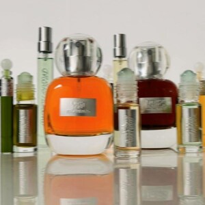 K&ouml;nnte beinhalten: Eine Sammlung von Glasparf&uuml;mflaschen mit silbernen Etiketten und durchsichtigen Verschl&uuml;ssen. Die mittlere Flasche enth&auml;lt eine leuchtend orangefarbene Fl&uuml;ssigkeit, w&auml;hrend andere bernsteinfarbene, gr&uuml;ne und dunkelbraune Fl&uuml;ssigkeiten enthalten.