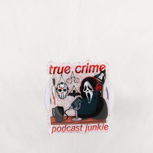 May include: A clear, glittery sticker with the words "true crime" and "podcast junkie" in red. The design includes a Ghostface character with headphones, a microphone, and horror-themed icons.