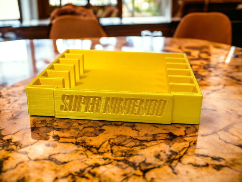 May include: A yellow plastic storage case with slots for video game cartridges. The case has the words "SUPER NINTENDO" printed on the front.