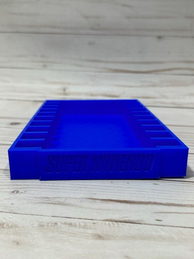 May include: A blue plastic storage case for Super Nintendo game cartridges. The case has 12 slots for cartridges and the words "SUPER NINTENDO" are embossed on the front.