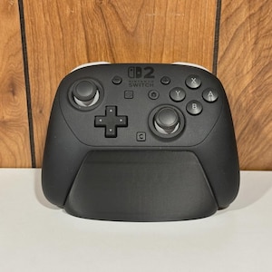 Op de afbeelding: Zwarte Nintendo Switch Pro Controller met witte accenten. De controller heeft een D-pad, analoge sticks en actieknoppen. Het Nintendo Switch-logo is zichtbaar. Een accessoire voor gaming.