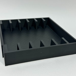 May include: Black plastic storage box with multiple compartments. The box is empty and has a square shape.