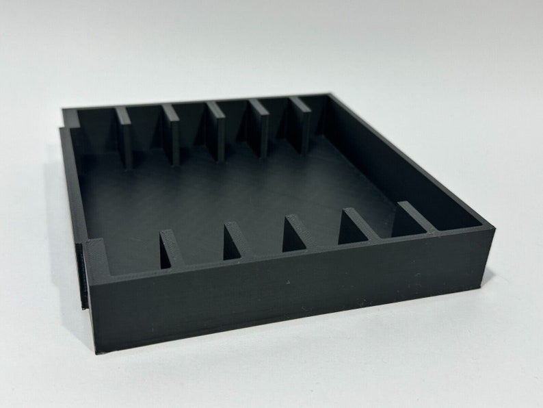 May include: Black plastic storage box with multiple compartments. The box is empty and has a square shape.