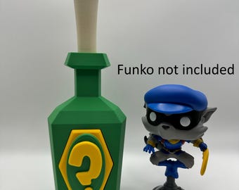 May include: A green bottle with a yellow question mark on the front. The bottle has a white top and is made of plastic. The bottle is next to a gray and blue figurine of a wolf wearing a blue hat. The text "Funko not included" is visible in the image.