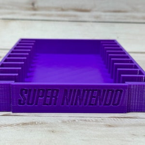 May include: Purple plastic storage case with 10 slots for Super Nintendo game cartridges. The case has the words "SUPER NINTENDO" printed on the front.