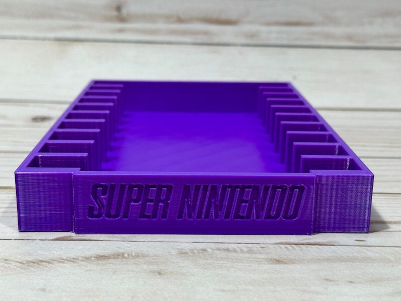 May include: Purple plastic storage case with 10 slots for Super Nintendo game cartridges. The case has the words "SUPER NINTENDO" printed on the front.