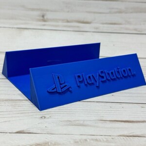 May include: A blue plastic stand with the PlayStation logo and the word "PlayStation" embossed on it.