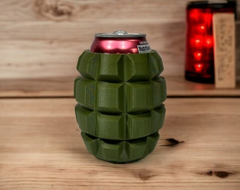 Puede incluir: Un enfriador de latas de color verde en forma de granada con una lata de refresco roja en su interior.