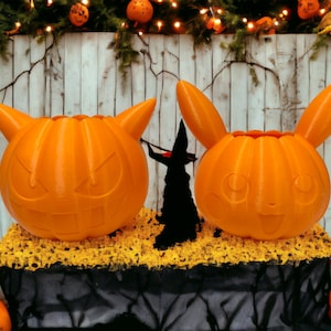 Puede incluir: Dos decoraciones de Halloween de color naranja en forma de calabaza con caras talladas. Una calabaza tiene forma de Pikachu y la otra tiene forma de demonio. Ambas calabazas están sobre una superficie negra con musgo amarillo.