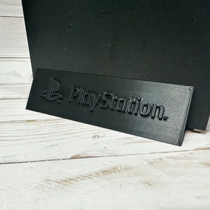 May include: A black plastic stand with the PlayStation logo embossed on it.