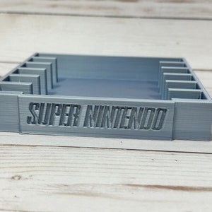 May include: A grey 3D printed Super Nintendo game cartridge holder with slots for multiple cartridges.
