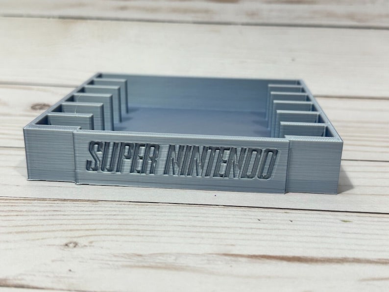 May include: A grey 3D printed Super Nintendo game cartridge holder with slots for multiple cartridges.