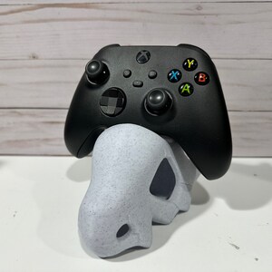 May include: A black Xbox controller with colored buttons sits on a white, speckled, 3D printed stand.