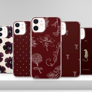 Może przedstawiać: Kolekcja etui na telefony o różnych wzorach. Etui mają wzory kwiatowe, grochy i motywy kokardek w kolorze białym i złotym na głębokim bordowym tle. Jedno etui ma złotą ilustrację lamparta i napis "the winner".