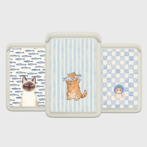 May include: Three decorative cases with cat illustrations. One case features a Siamese cat with a fish pattern background. Another shows an orange tabby cat holding fish, set against blue stripes. The third case has a cat in a hat on a blue checkered background.