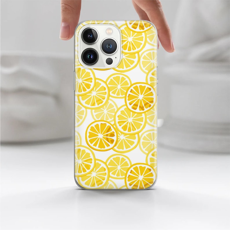 May include: A clear phone case with a pattern of yellow lemon slices on a white background. The case has a cutout for the camera lens.