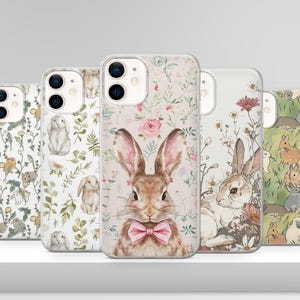 May include: Five phone cases featuring a floral design and a bunny rabbit illustration. The cases are clear and showcase the phone's camera lens. The bunny rabbit is wearing a pink bow tie.