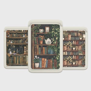 May include: Three cream-colored phone cases with a bookcase design. The cases feature illustrations of bookshelves filled with books, plants, and decorative items. One case shows a black cat, another a teapot, and the third a full bookshelf.
