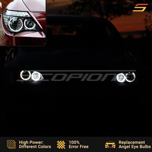 Może przedstawiać: Zbliżenie na reflektory samochodu z białymi pierścieniami angel eye. Reflektory są włączone, a pierścienie są podświetlone. Pod obrazem widnieje tekst "High Power: Different Colors", "100% Error Free" i "Replacement Angel Eye Bulbs".