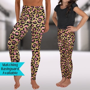 May include: Matching pink and gold leopard print leggings for adults and children. The leggings have a high waist and are made of a stretchy, comfortable fabric. "Matching Rashguard Available" is written on a blue banner.