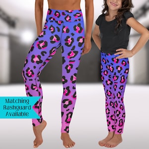 May include: A pair of purple and pink ombre leggings with a leopard print pattern. The leggings are shown on two people, one adult and one child. The text "Matching Rashguard Available" is in a blue box at the bottom left of the image.