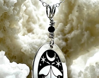 May include: A silver necklace with a black oval pendant featuring a moon, stars, and a moth design.
