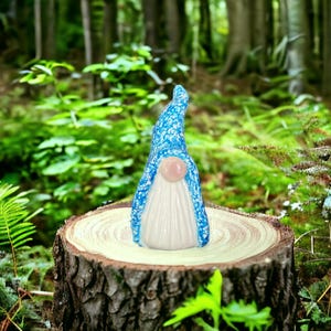 May include: A whimsical garden gnome figurine with a blue speckled hat and a white beard. The gnome has a pink nose and is standing on a tree stump. The background is a lush green forest.